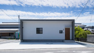 白い塗り壁の四角い家。軒と日よけの壁がグレーでオシャレな外観。格子の四角い窓がオシャレ。 be-plusパッシブデザインの家。