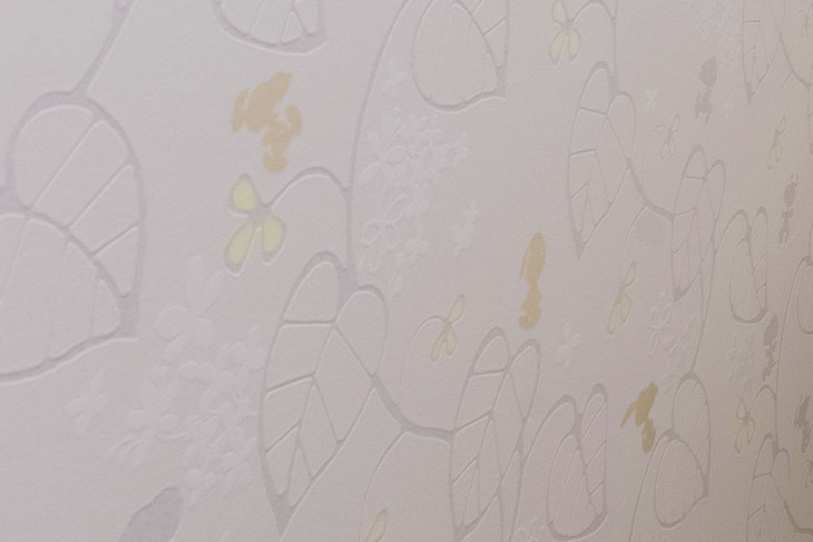 サンゲツ壁紙ＲＥ５１５６９は、オフホワイトのベースにシルバーと白の光沢ある植物が描かれている。ベージュのスヌーピーとイエローの小さな❀がアクセントとなり華やかさを演出している。