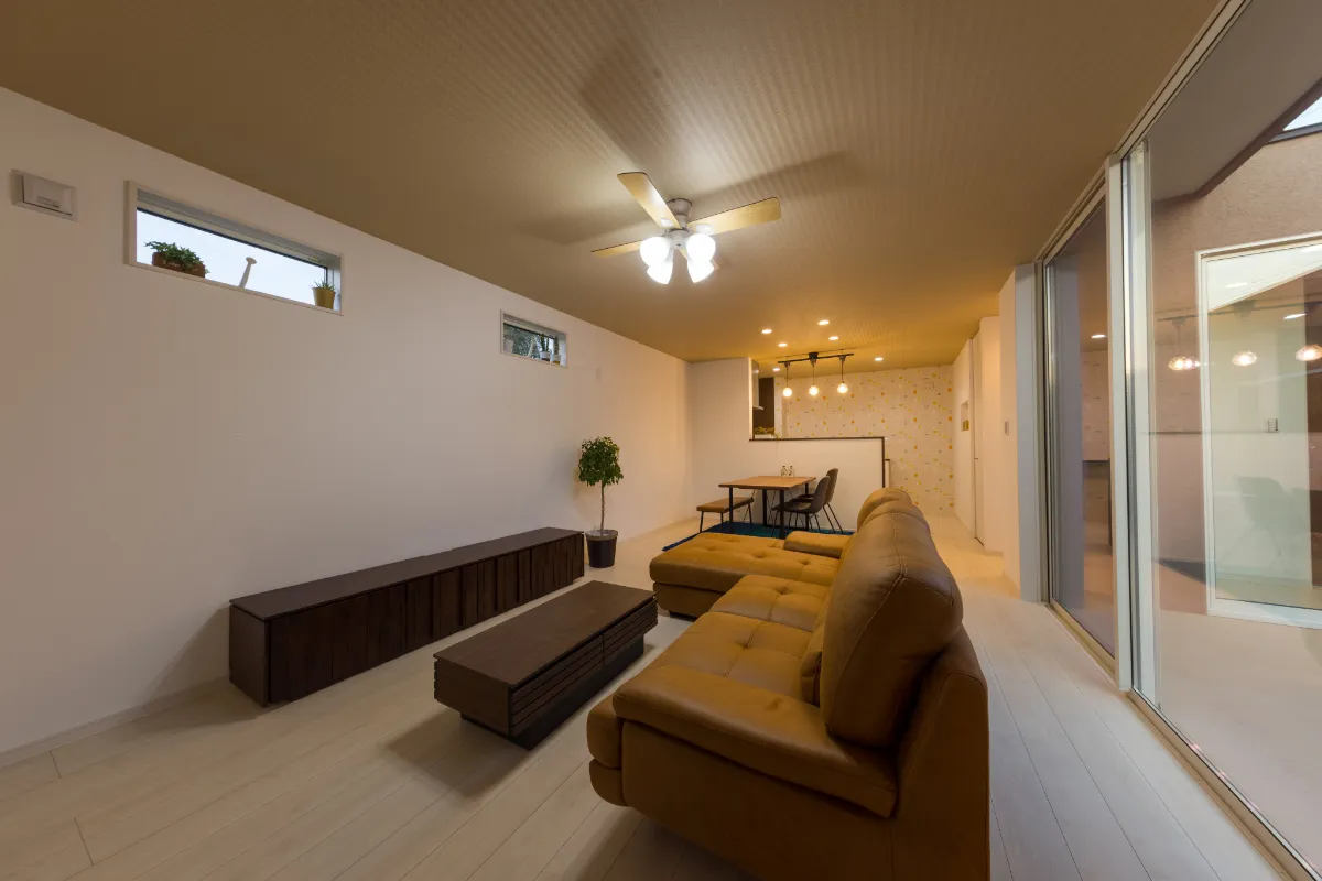 夜のリビングルーム、天井のファンライトが明るく照らし、ブラウンのレザーソファと木製ローテーブルが映える空間