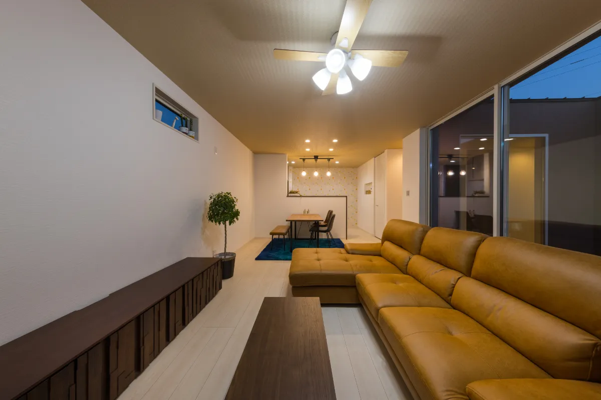 間接照明と天井ファンライトに包まれた夜のリビング、観葉植物がアクセントの落ち着いた室内