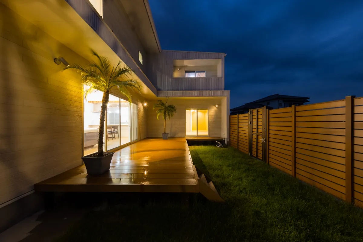 照明に照らされたヤシの木とフェンスがリゾート感を強調する夜のテラス全景