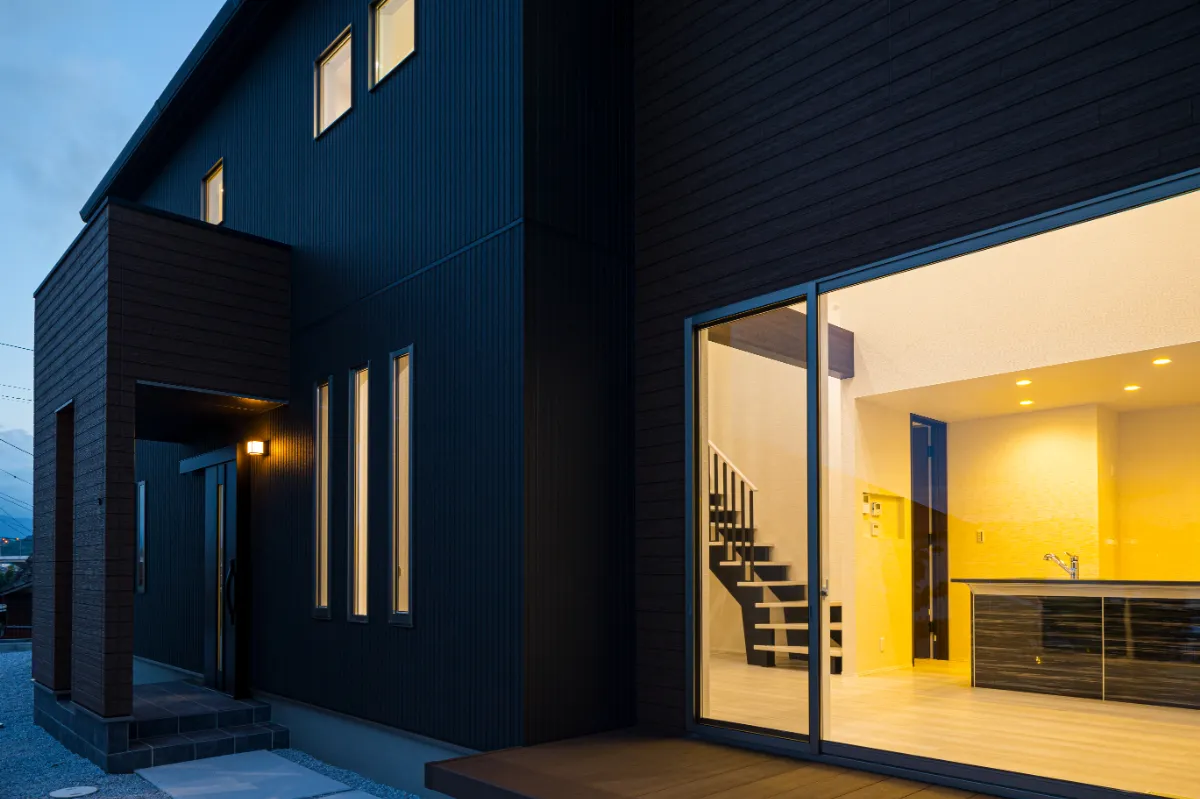室内の明かりが外へ漏れる、吹き抜け階段が見える夕暮れ時の外観