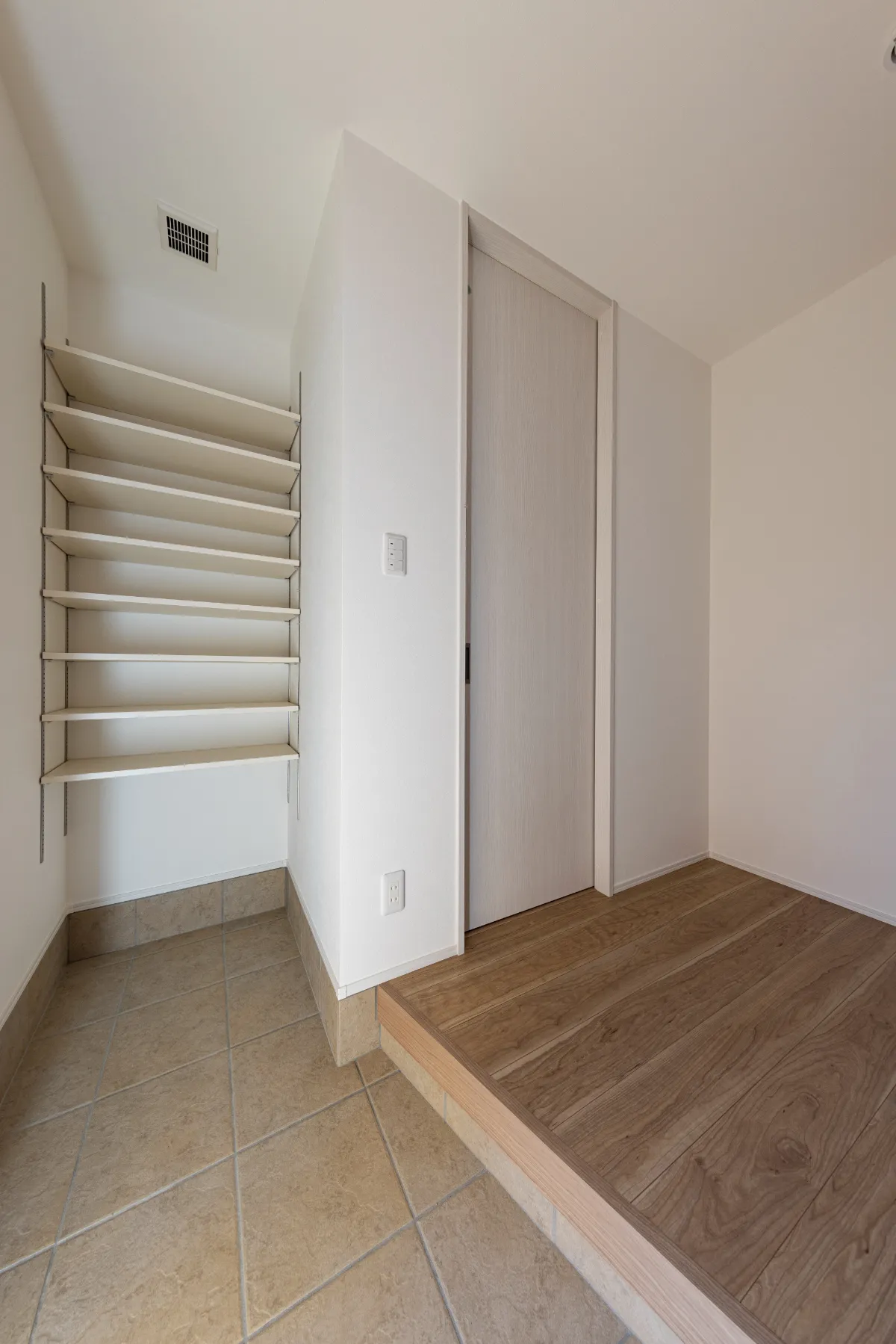 明るいタイル床と木目の上がり框が調和する玄関