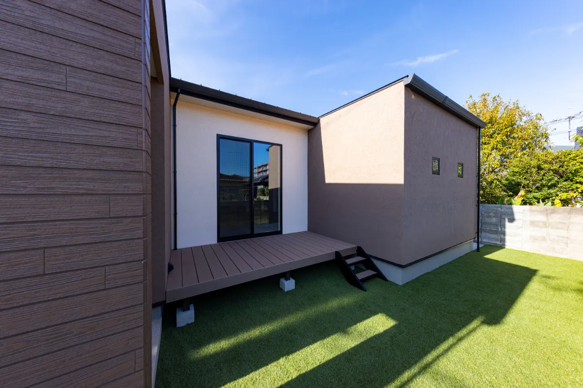 芝生の中庭に面したウッドデッキと塗り壁外壁