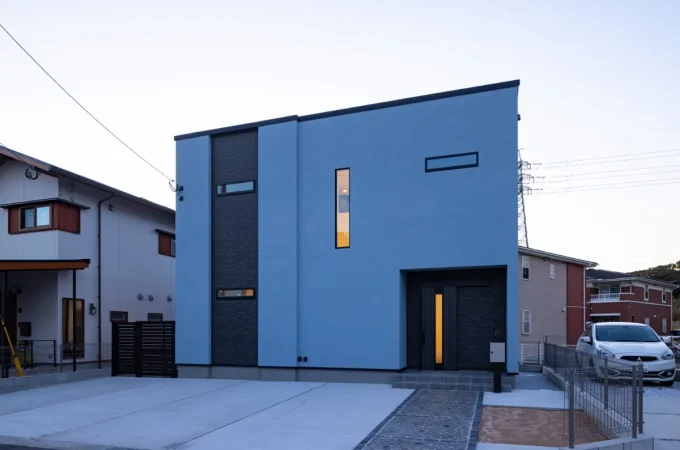 ブルーグレーの塗り壁とブラックの縦ラインが印象的な、スタイリッシュな外観の二階建て住宅
