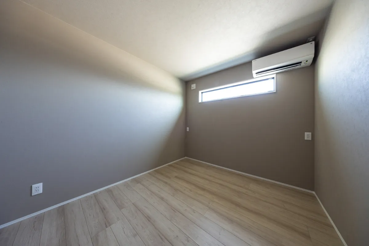 落ち着いたブラウングレーのアクセントクロスと木目フローリングが調和する、シンプルで心安らぐ洋室