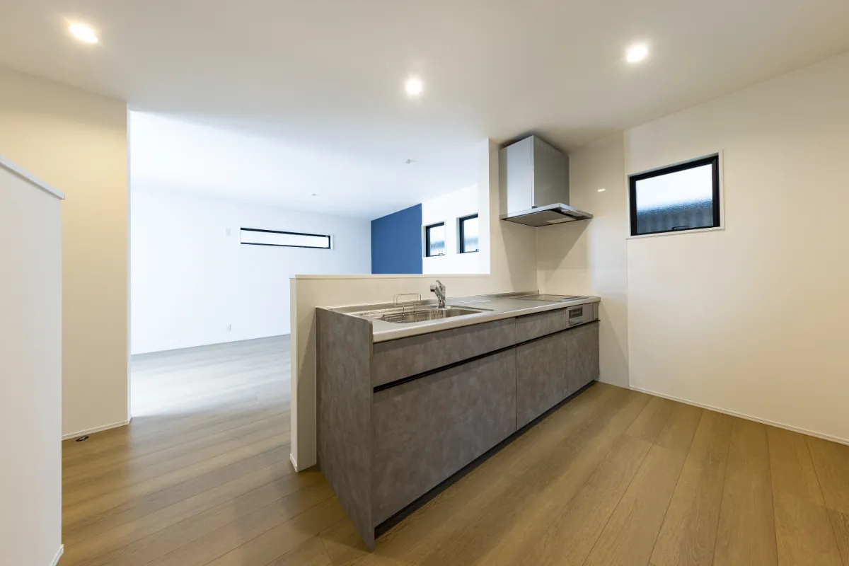 グレーのフラットなカウンターとシンプルな換気フードが特徴の対面式セミオープンキッチン