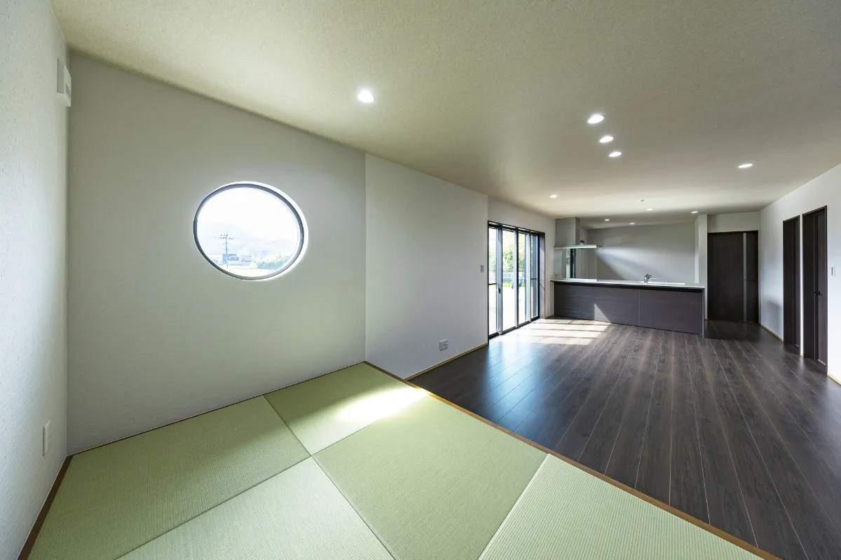 円形の窓からやわらかな自然光が差し込む小上がりの畳スペースと広々としたリビング