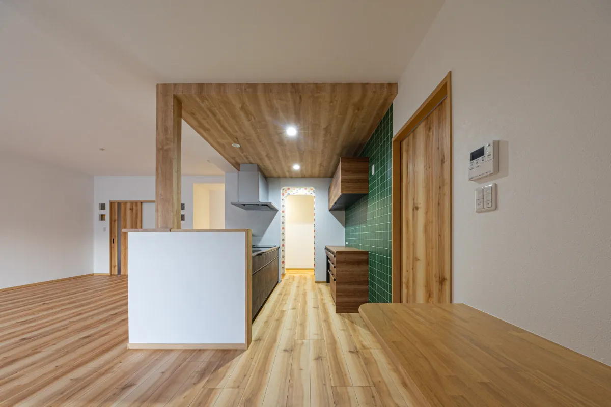 木目天井とグリーンタイルの組み合わせが目を引くキッチン。奥のアーチ開口が空間にやさしいリズムを加えています。