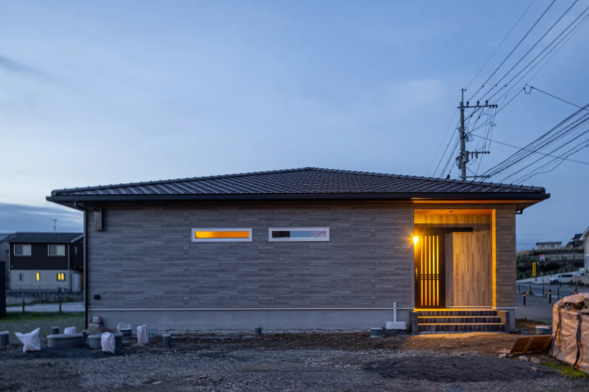 玄関ポーチにあたたかな灯りがともる夕景の外観。軒天の木目がやさしく映え、落ち着いた雰囲気に包まれています。