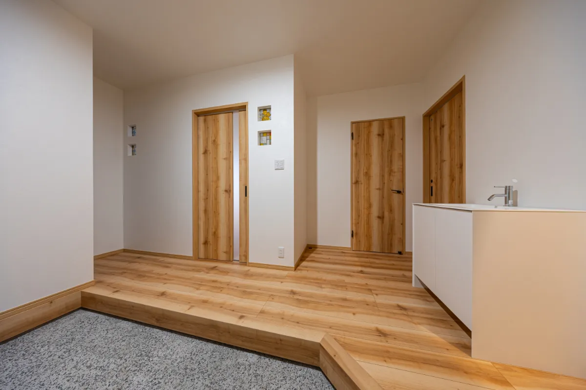 木目の床と白い壁でまとめた明るい玄関ホール。段差を設けた上がり框が空間にメリハリをつくり、奥行きを感じさせます。