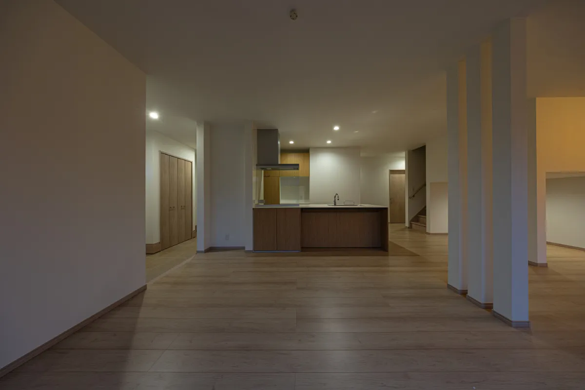 リビング奥からキッチンを望む夜のLDK。格子と天井の照明が空間にリズムを生み、家族が自然と集まる心地よい広がりを感じさせます。