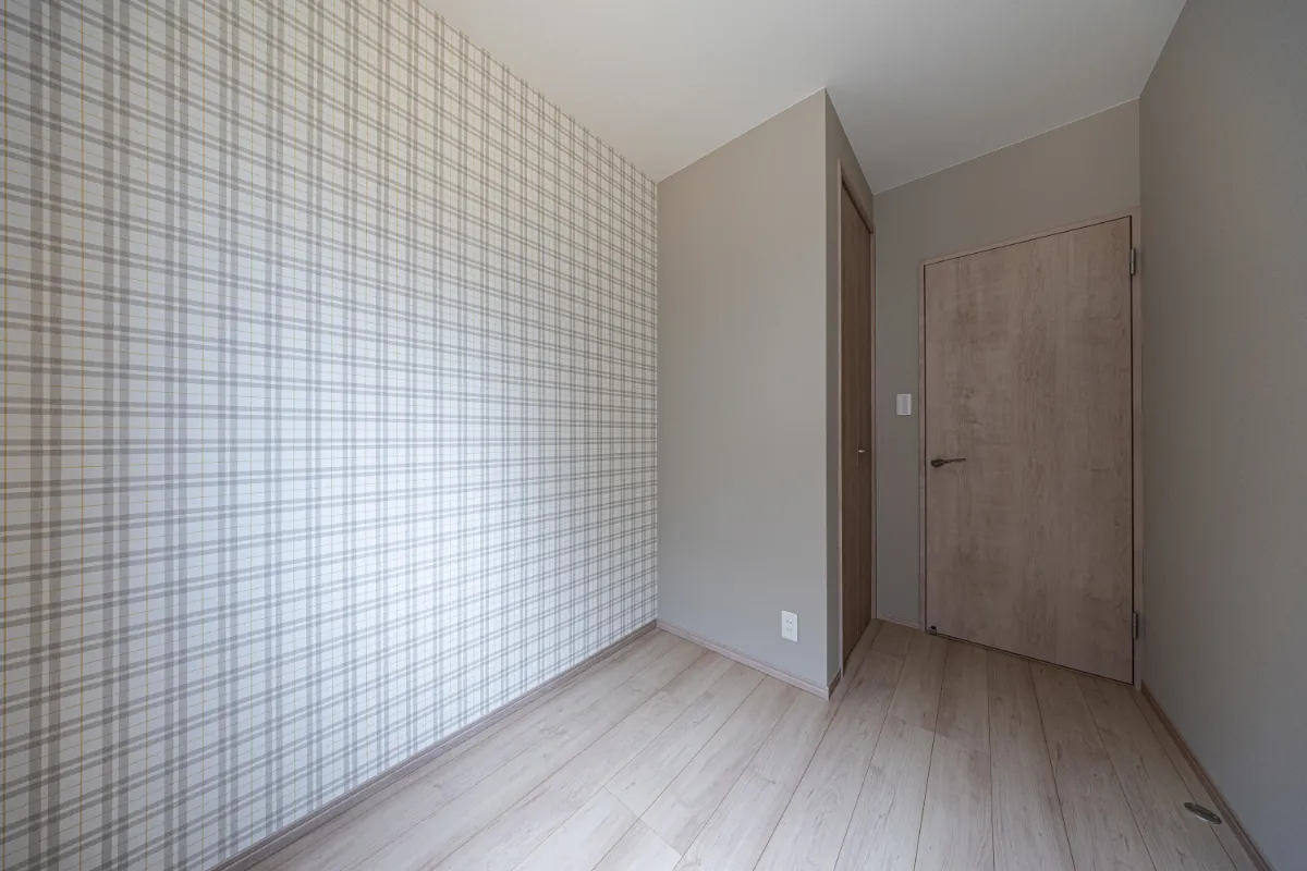 チェック柄のアクセントクロスが印象的な洋室。落ち着いた色味の壁と木目の扉がほどよく調和し、個性を感じられる空間になっています。