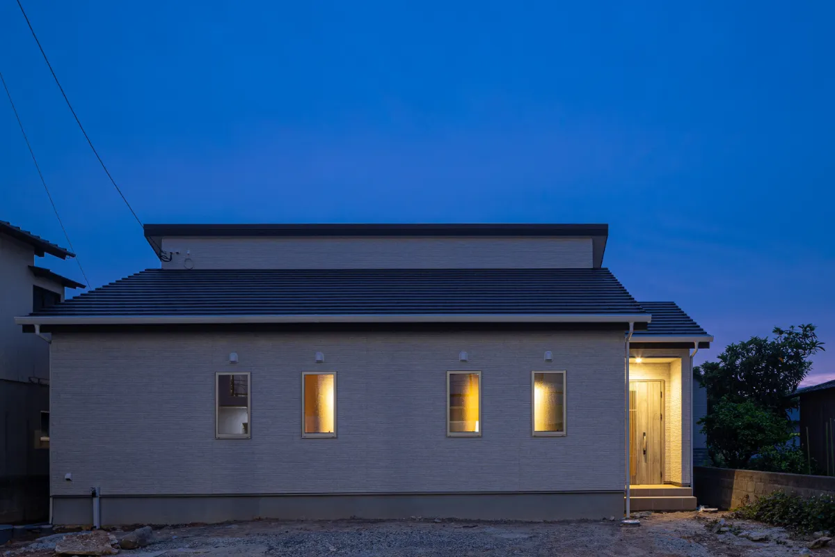 室内のあかりがやさしく漏れる夕景の外観。窓越しの灯りと玄関まわりの照明が、帰宅時をあたたかく迎えます。