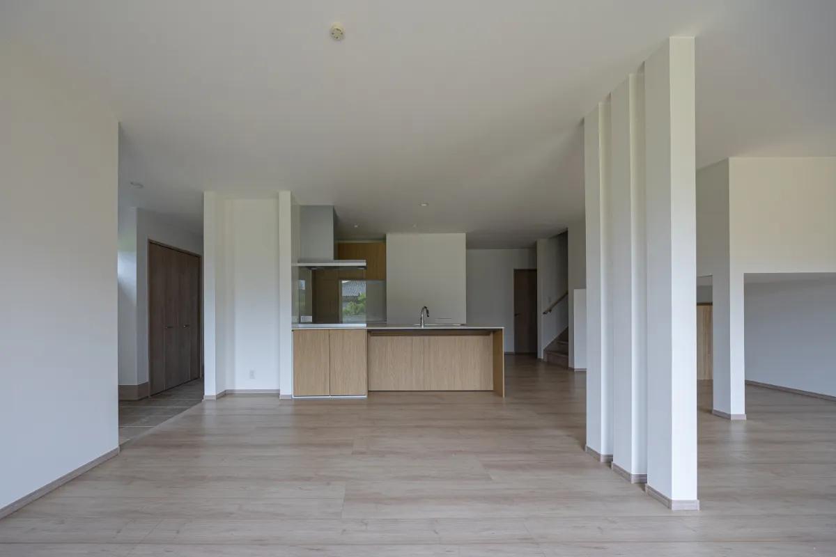 キッチンを中心に広がる開放的なLDK。床から天井まで伸びるスリット柱が空間をやさしく仕切り、明るい木目の床と白い壁がすっきりとした印象を与えています。