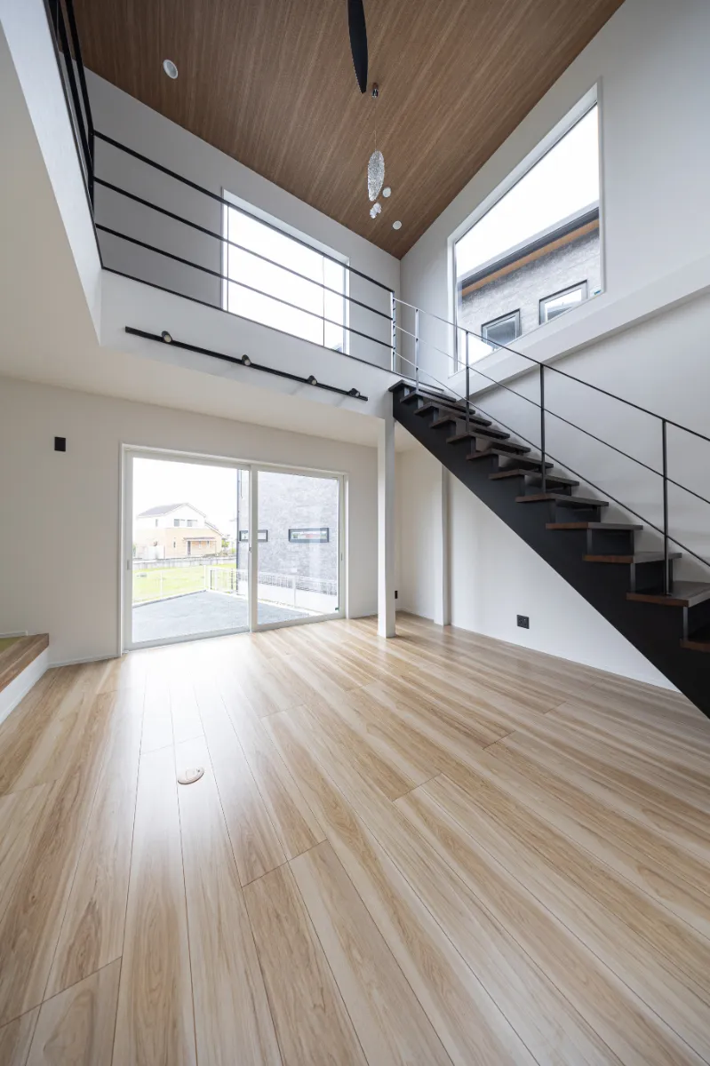 吹き抜けと2階ホールがつながるリビング空間。天井の木目と大きな窓がアクセントとなり、上下階に光と風が行き渡る設計です。