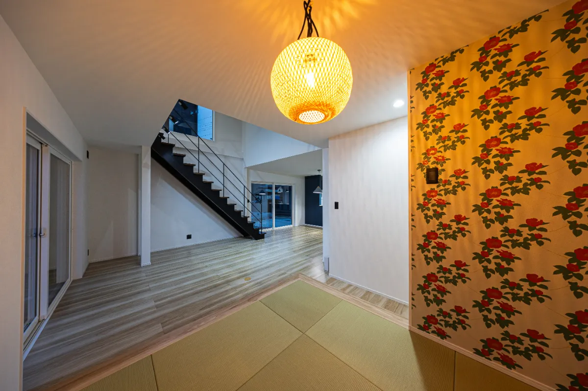 畳スペースから見た夜のリビング。階段まわりの照明と木目の床が調和し、あたたかみのある空間が広がります。