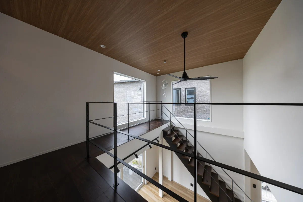 2階ホールから見下ろす吹き抜け空間。黒のアイアン手すりと木目天井がアクセントになり、上下階がゆるやかにつながる開放的な設計です。