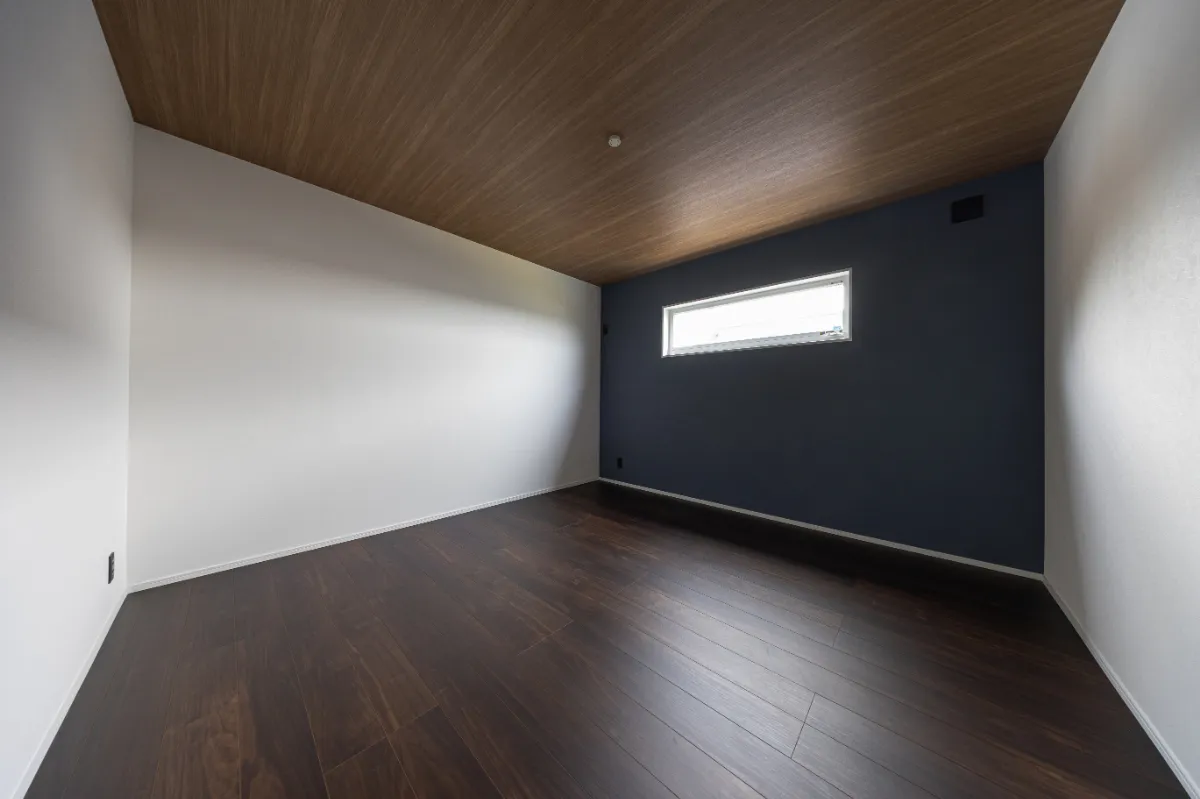 ネイビーのアクセントクロスと木目天井を組み合わせた洋室。落ち着いた色合いの中に素材感を取り入れ、くつろぎやすい空間に仕上げています。