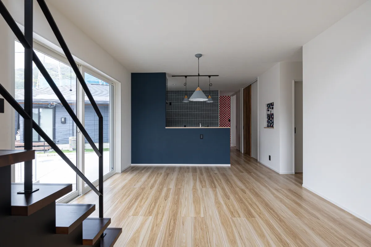 ネイビーの腰壁がアクセントになったLDKとキッチン空間。リビング階段と大きな窓からの光で、開放感のある明るい室内に仕上がっています。