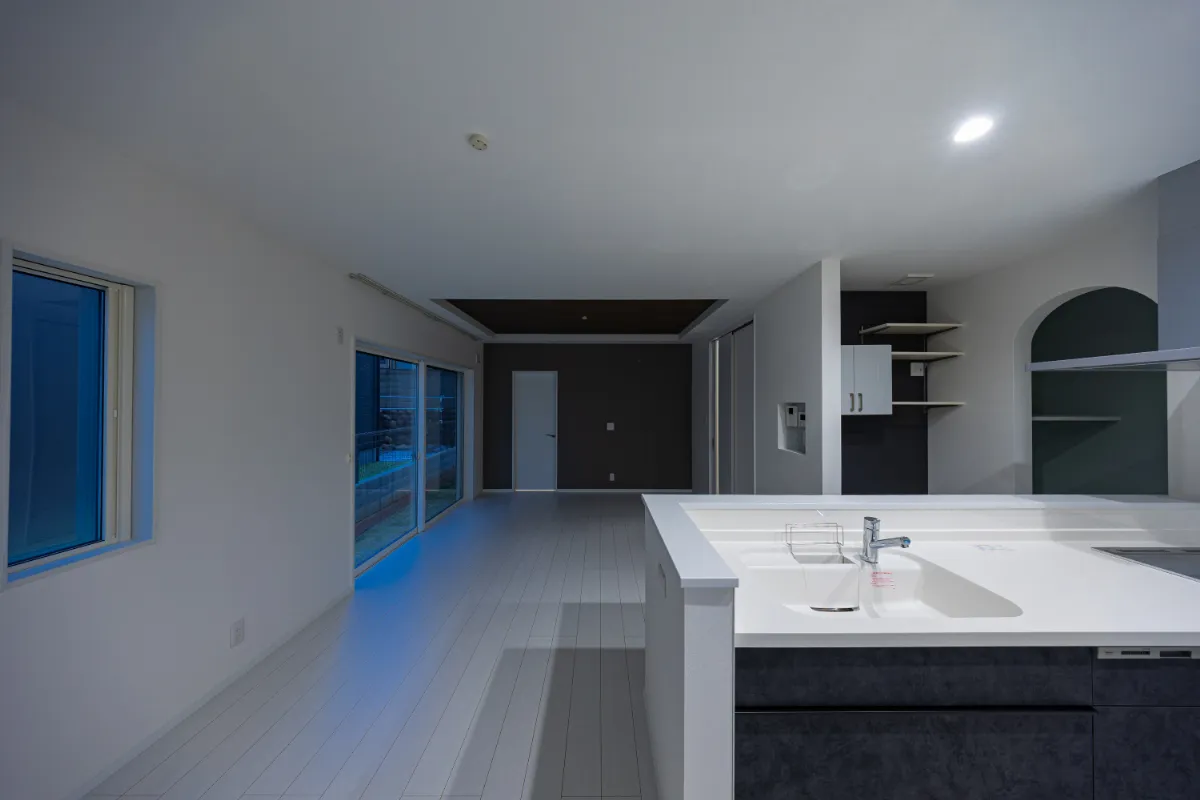 シンク側からLDKを望むキッチン。間接的に入る光と落ち着いた配色が、夜も心地よく過ごせる雰囲気をつくっています。