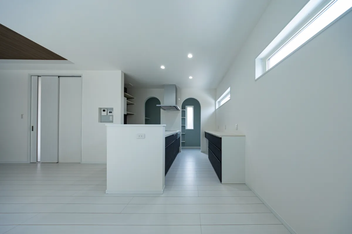 昼間のキッチン全体。白い床と壁に濃色の収納を合わせ、明るさの中にほどよいメリハリを持たせた空間です。